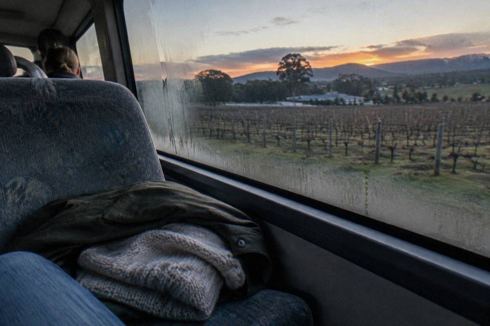 A folded jumper and light jacket resting on a tour bus seat next to a denim-clad leg.