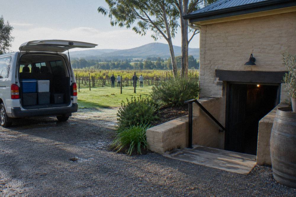 A small tour van parked beside a cellar door building surrounded by vineyards