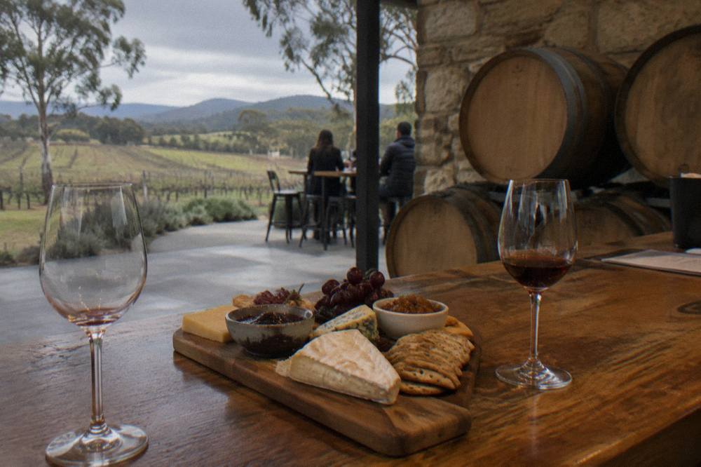 A fromage platter with crackers and preserves set beside glasses of fortified wine on a cellar door bar