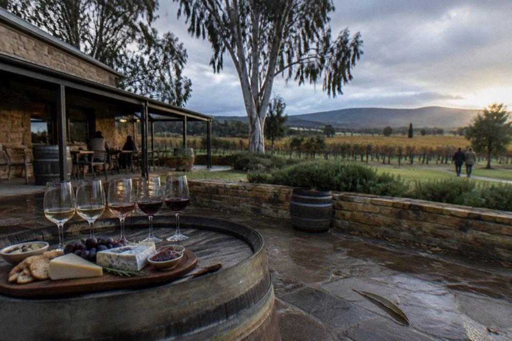 A small group of wine glasses lined on a barrel top beside a platter in a winery courtyard