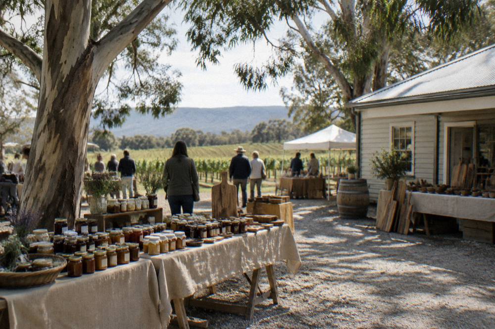 Handmade goods displayed on trestle tables under trees beside a winery building