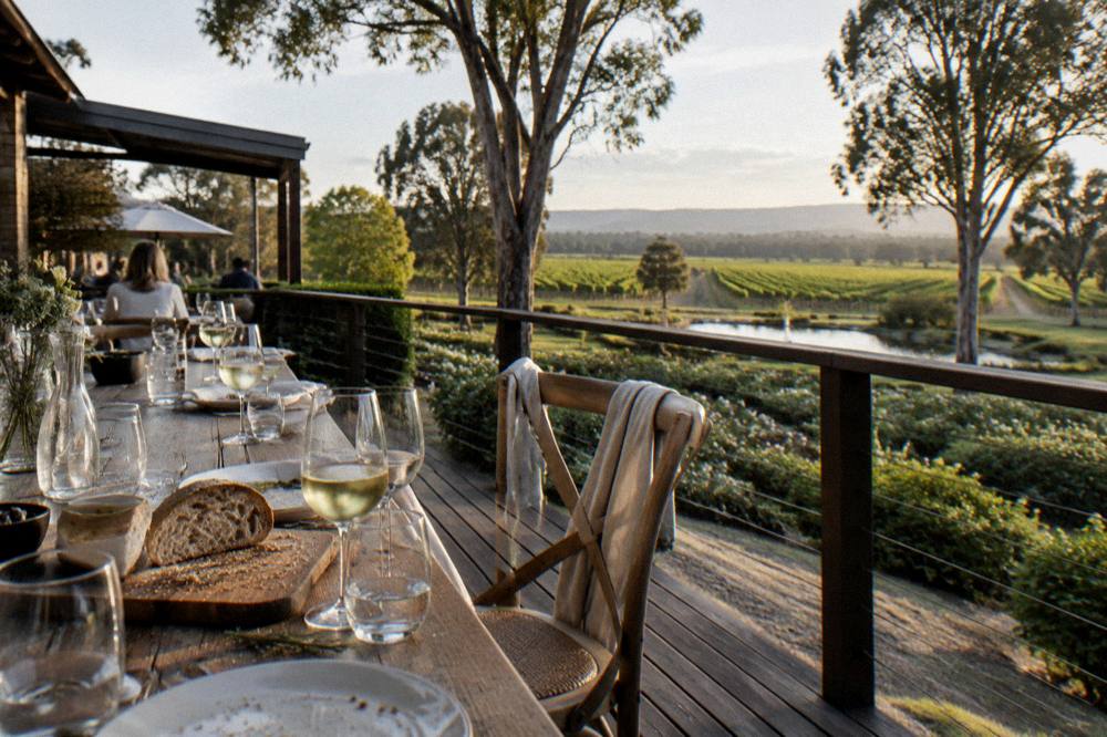 Long lunch table set with wine glasses on a deck overlooking vines