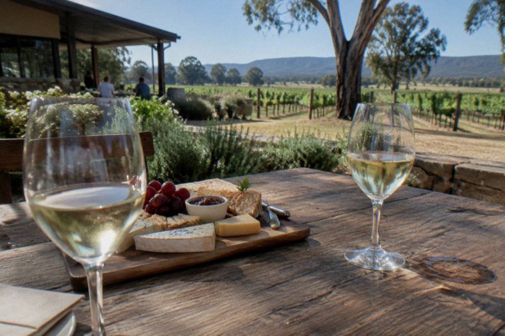 A tasting platter of cheese and crackers beside glasses of white wine on a wooden table
