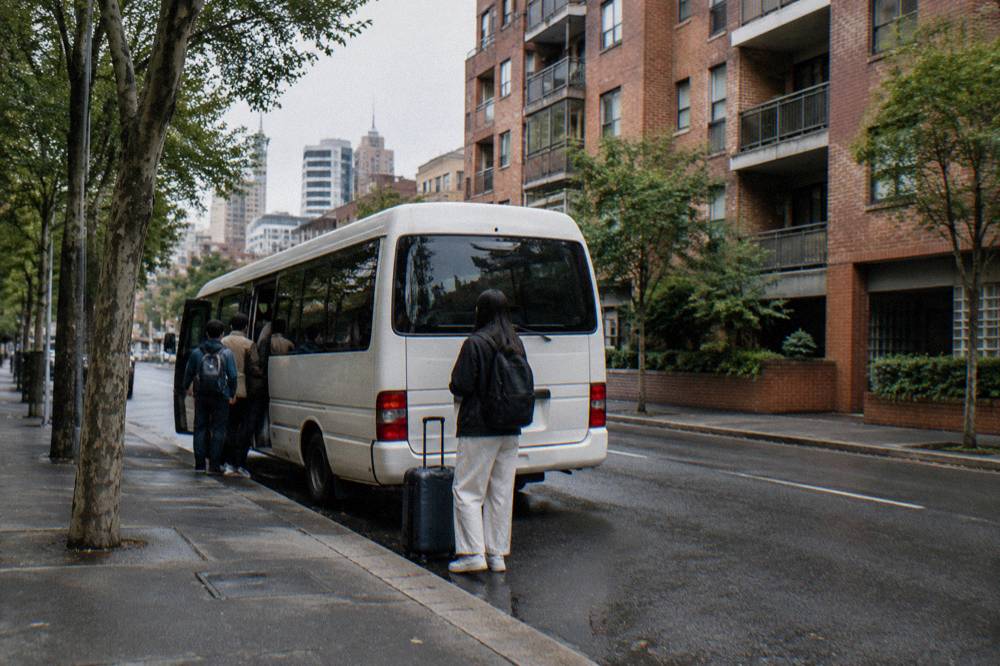 A tour minibus parked on a country road beside vineyard rows at midday