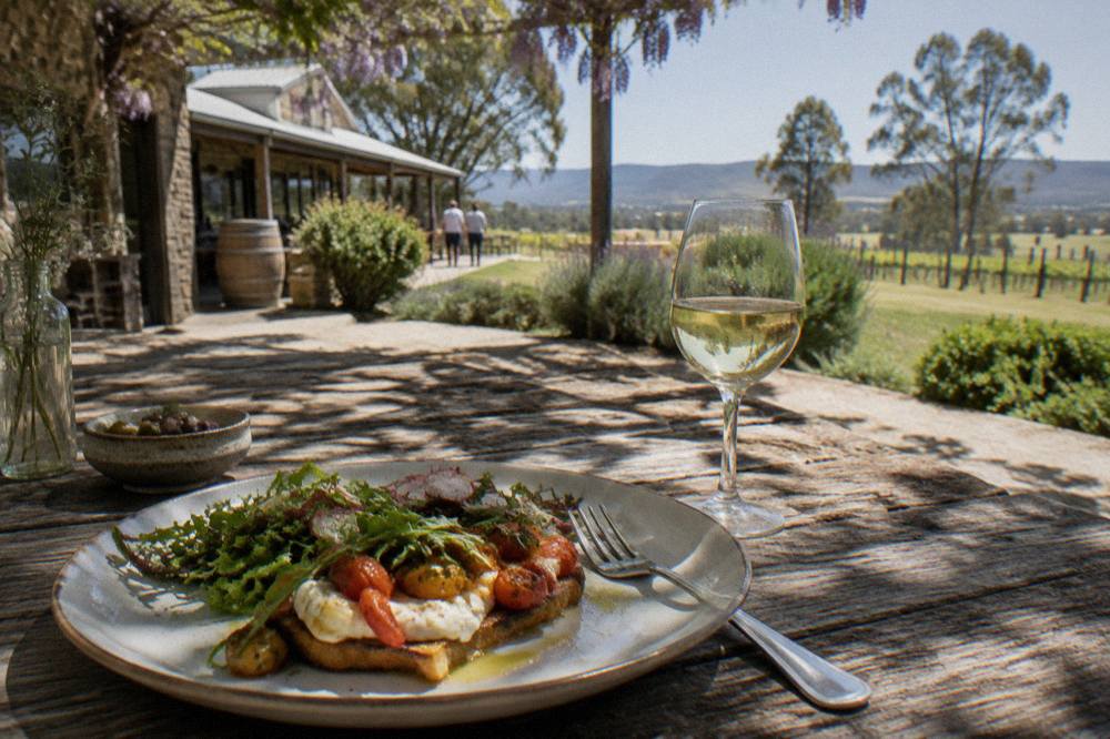 A plated lunch of local produce on a wooden table beside a glass of white wine