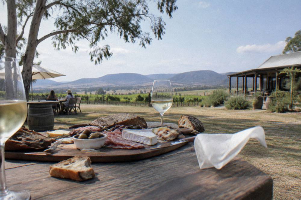 A grazing box of cheese, meats and bread on a table among vineyards
