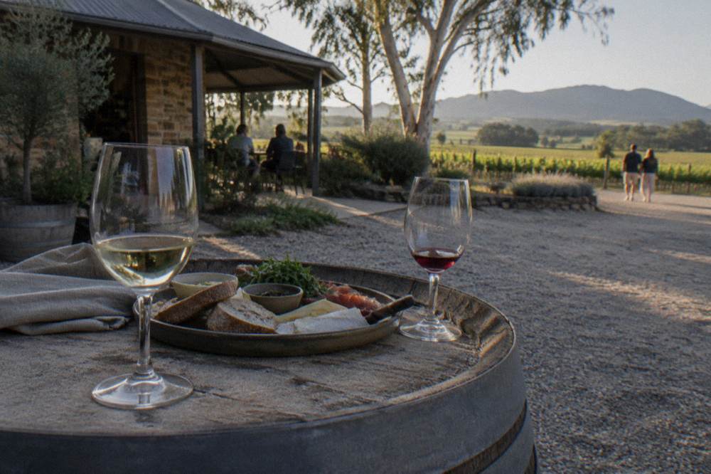 Two wine glasses and a shared lunch plate on a barrel top outside a cellar door