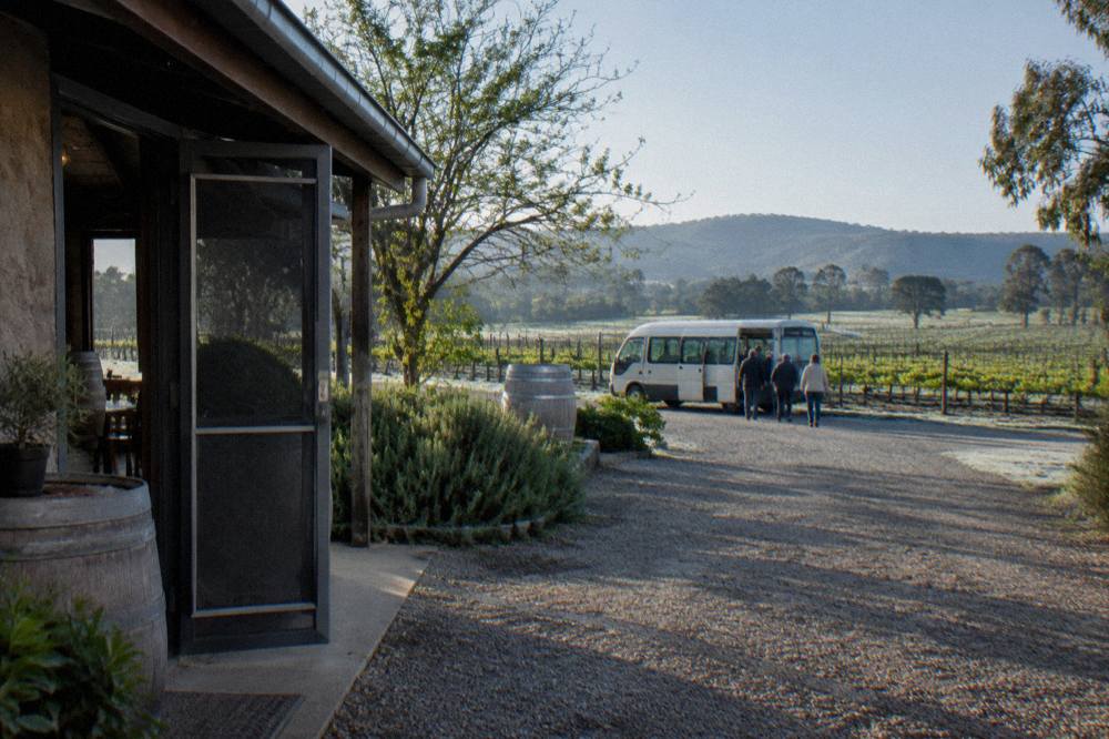 Small tour van parked beside a rustic cellar door among vineyards