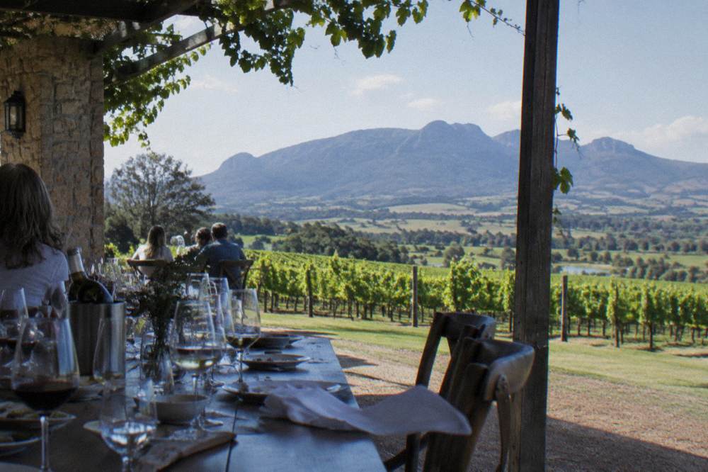 A long lunch table set with wine glasses on a verandah overlooking vineyards