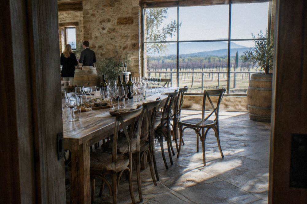 A long table set for a wine tasting with glasses and cheese boards in a light-filled cellar door room