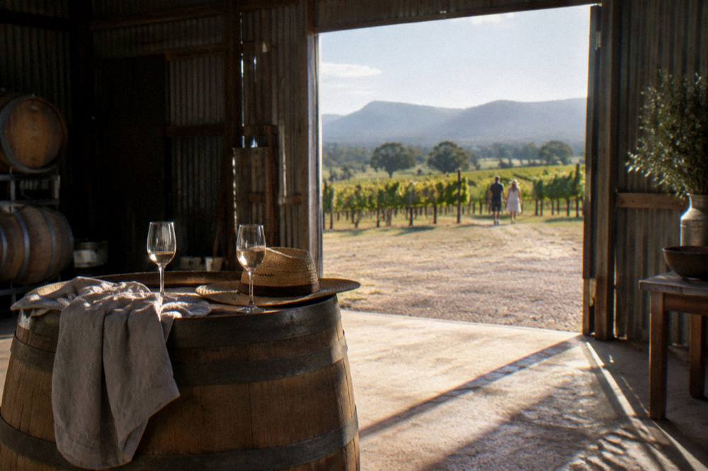 A casual outdoor tasting table with wine glasses set on a barrel in a cellar shed